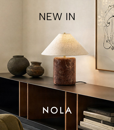 Stolová lampa Nola s červenohnedým mramorovým podstavcom a kužeľovitým ľanovým tienidlom na tmavej komode. Text: „Novinka – Nola“.