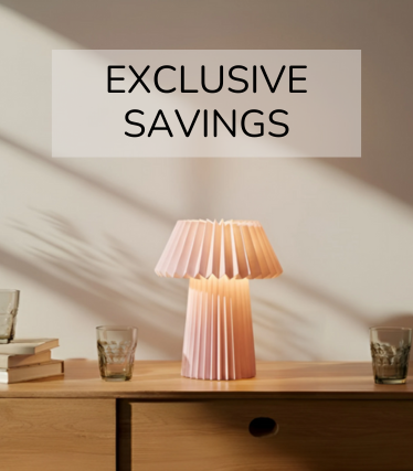 Bledoružová stolová lampa na drevenom príborníku, obklopená pohármi a knihami v teplom slnečnom svetle.