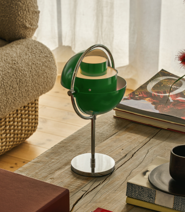 Zelená stolová lampa Multi-Lite s chrómovanou základňou na drevenom stole vedľa kníh.